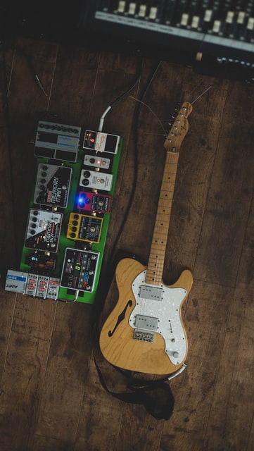 E-Gitarre neben Pedalboard auf Parkettboden im Recording Studio.